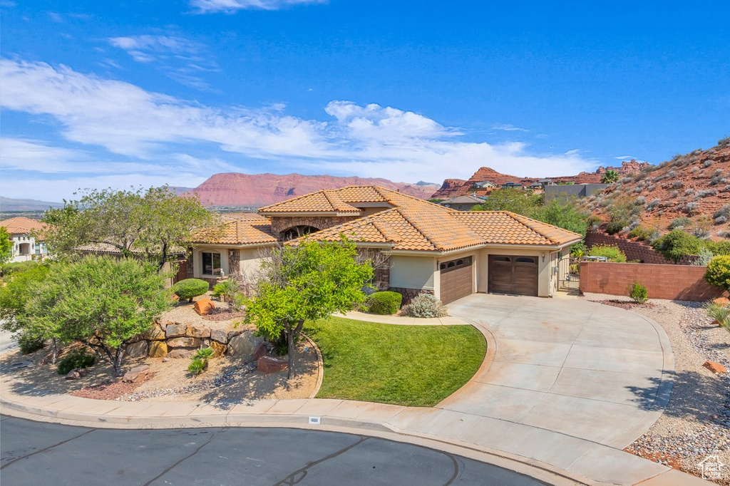 Mediterranean / spanish house with an attached garage, stucco siding, concrete driveway, a tile roof, and a mountain view