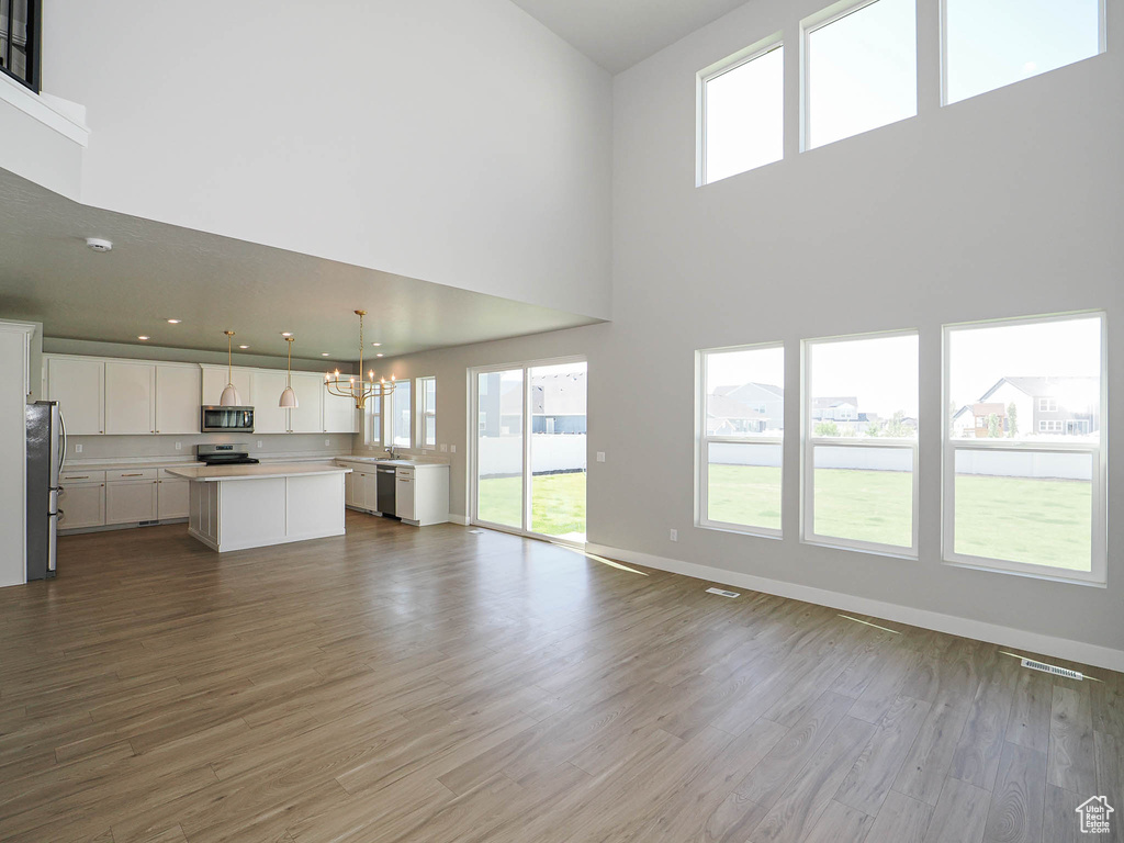 Unfurnished living room featuring a chandelier, a towering ceiling, and dark wood-style flooring