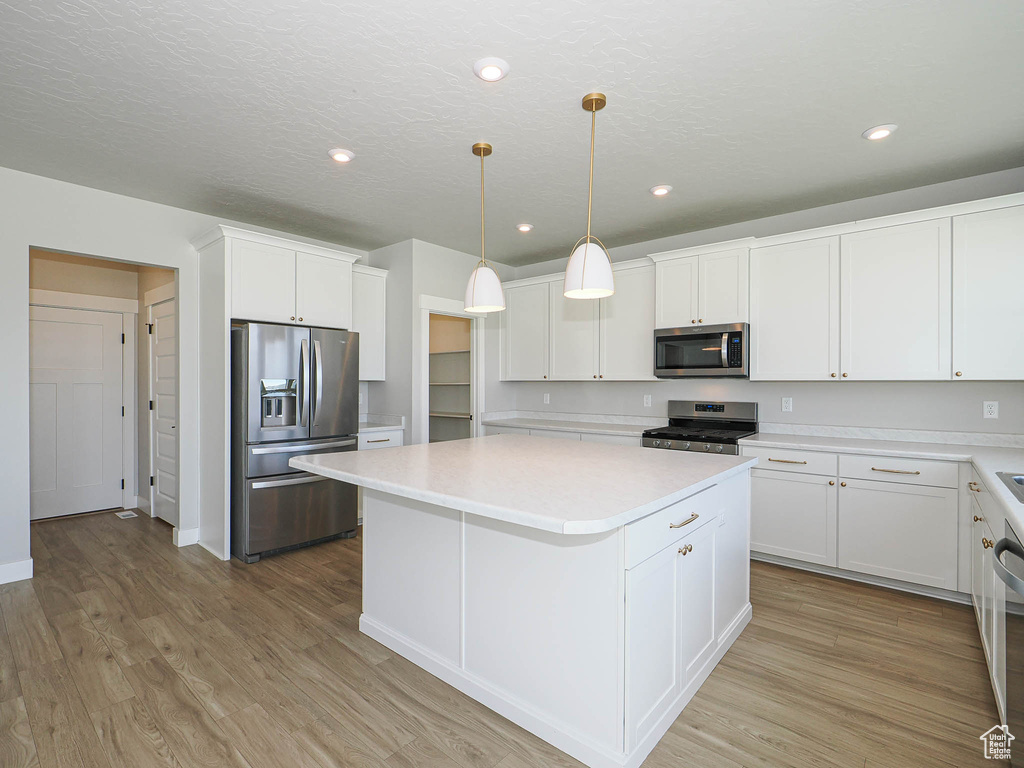 Kitchen with stainless steel appliances, a kitchen island, light countertops, white cabinetry, and light wood-style flooring