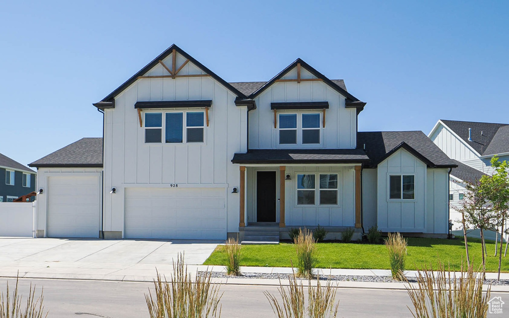 View of front facade featuring board and batten siding, concrete driveway, a front lawn, and roof with shingles