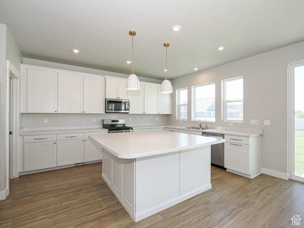 Kitchen featuring stainless steel appliances, light wood-type flooring, white cabinetry, a center island, and recessed lighting
