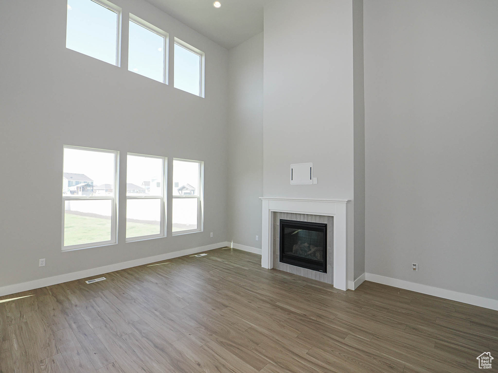 Unfurnished living room with a high ceiling, wood finished floors, and a tiled fireplace