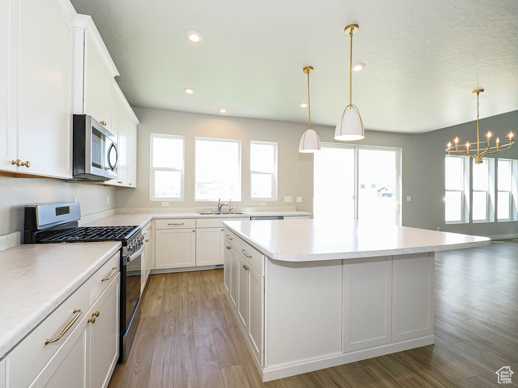 Kitchen featuring stainless steel appliances, a chandelier, a kitchen island, white cabinets, and light countertops
