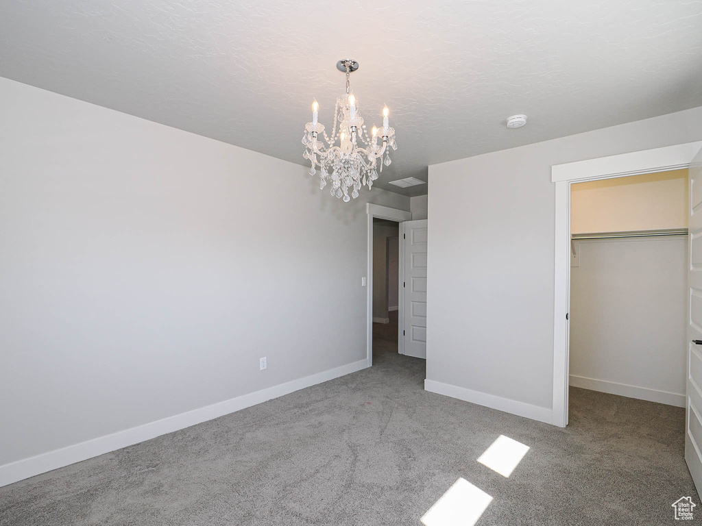 Unfurnished bedroom with a chandelier, carpet, and a walk in closet