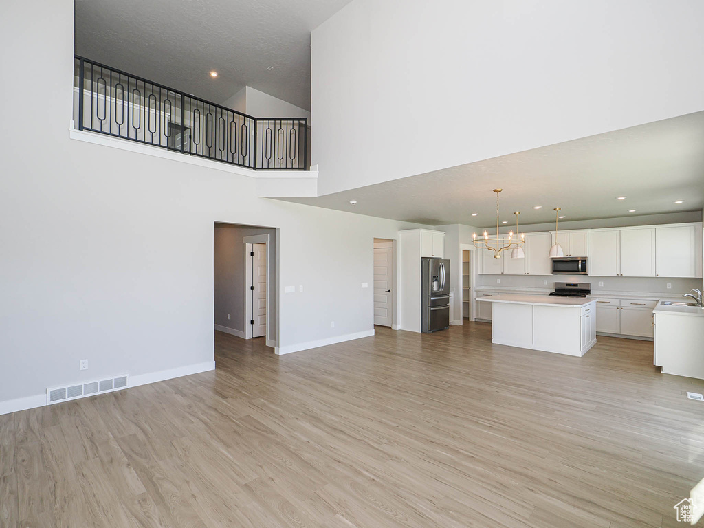 Unfurnished living room featuring a chandelier, light wood-style flooring, a high ceiling, and recessed lighting