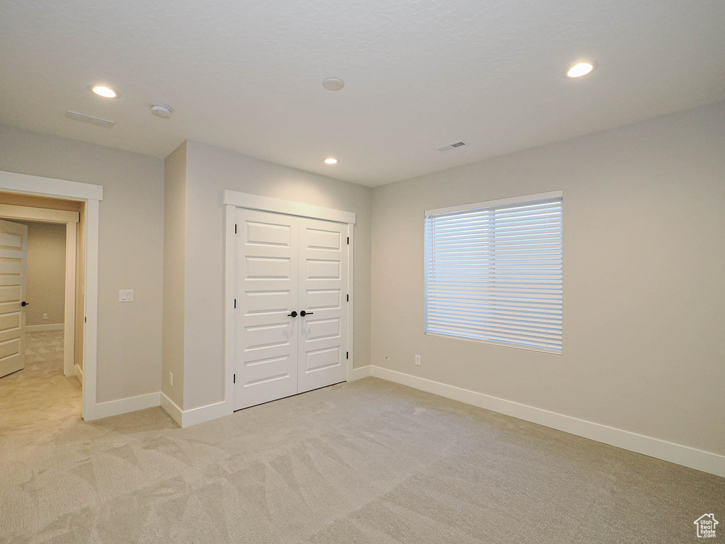 Unfurnished bedroom featuring light colored carpet, recessed lighting, and a closet