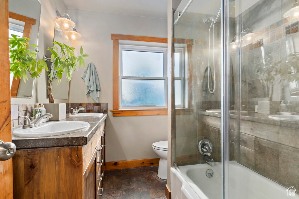 Full bathroom featuring double vanity, stone finish floors, and bath / shower combo with glass door