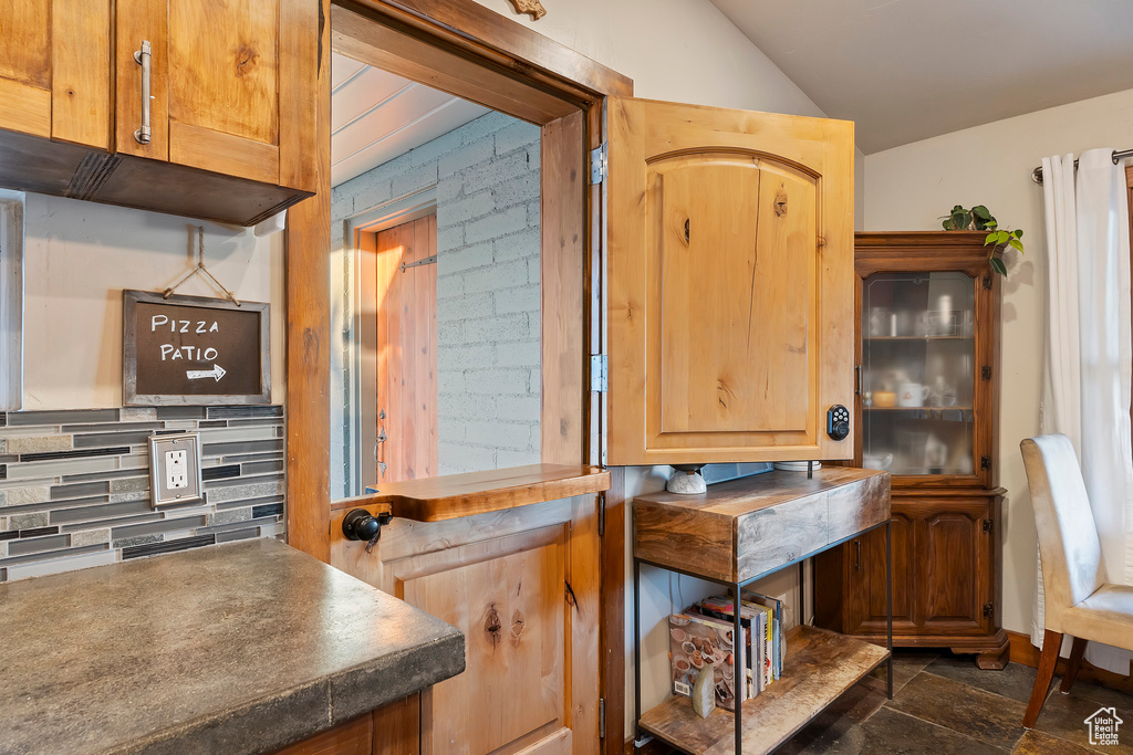 Bar featuring backsplash, vaulted ceiling, and dark stone finish flooring