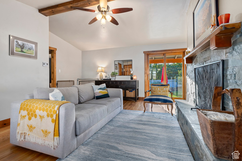 Living room featuring wood finished floors, a ceiling fan, and a fireplace with raised hearth