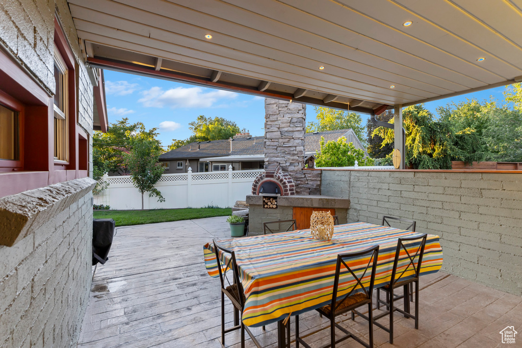 Fenced backyard featuring an outdoor fireplace, a deck, outdoor dining space, and a patio