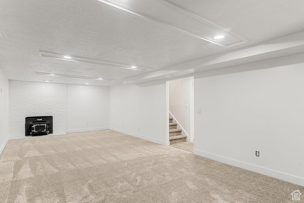 Finished below grade area featuring a wood stove, light colored carpet, stairway, a textured ceiling, and recessed lighting