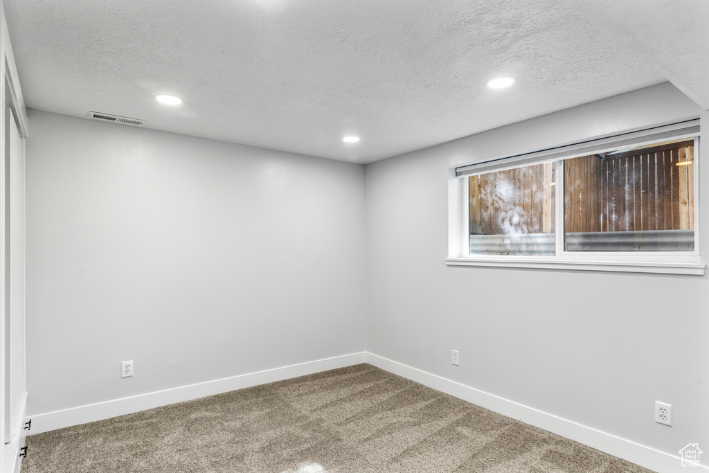 Carpeted empty room with a textured ceiling and recessed lighting