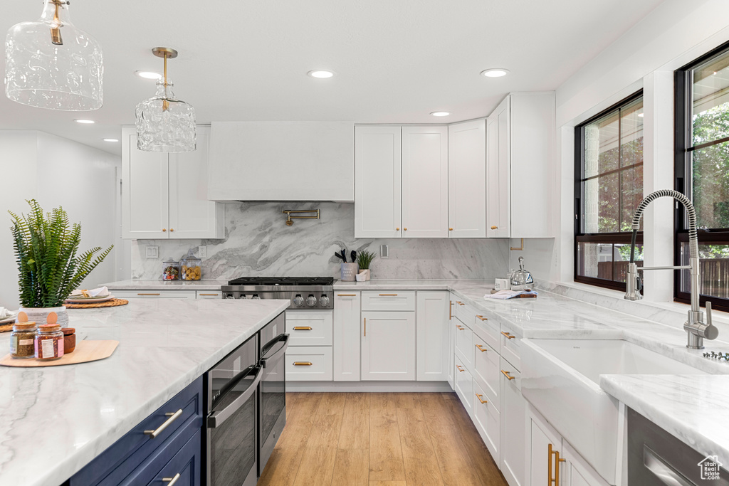 Kitchen featuring blue cabinetry, custom range hood, white cabinetry, light wood-style floors, and recessed lighting