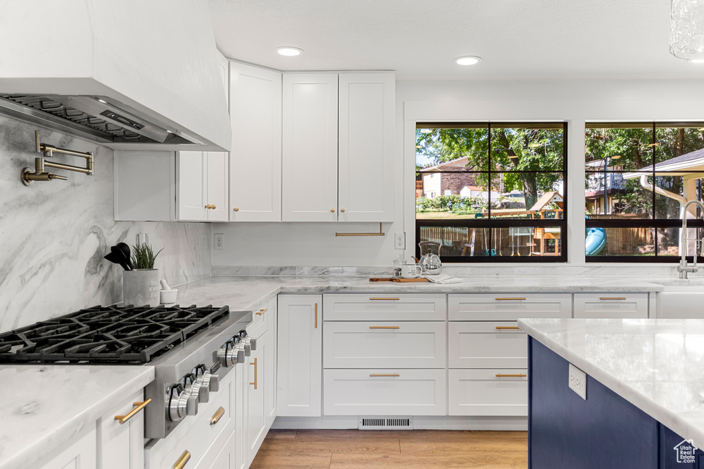 Kitchen featuring stainless steel gas cooktop, exhaust hood, white cabinets, light wood-style floors, and light stone counters
