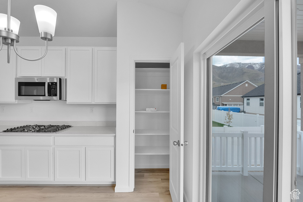 Kitchen featuring stainless steel appliances, light wood-type flooring, white cabinets, hanging light fixtures, and light countertops
