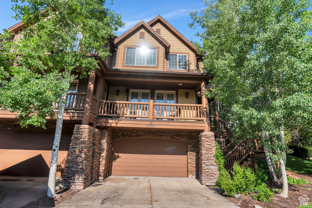View of front facade featuring concrete driveway, an attached garage, stone siding, and a porch