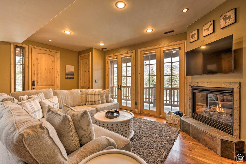 Living area with wood finished floors, recessed lighting, a premium fireplace, and french doors