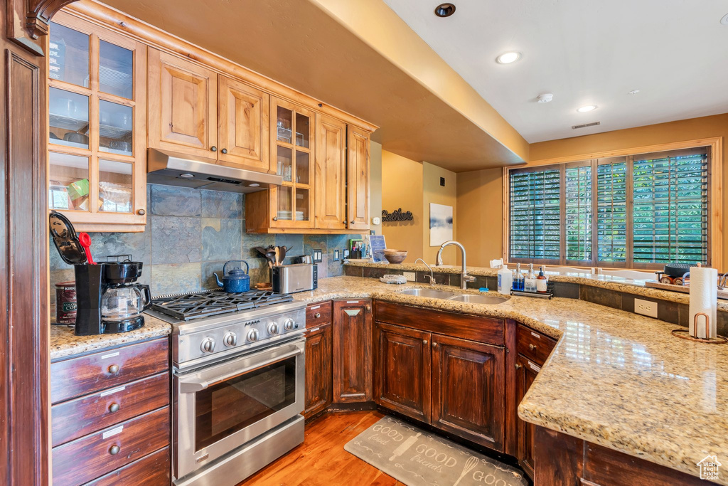 Kitchen featuring gas stove, under cabinet range hood, light stone countertops, decorative backsplash, and light wood-style flooring
