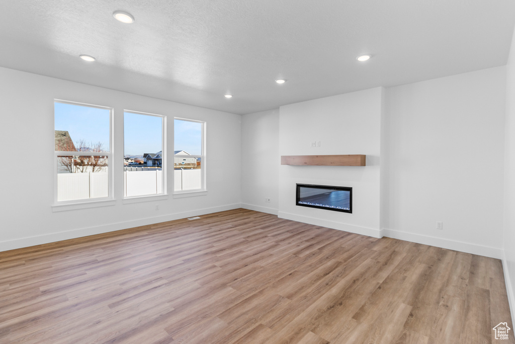Unfurnished living room with a glass covered fireplace, light wood-type flooring, and recessed lighting