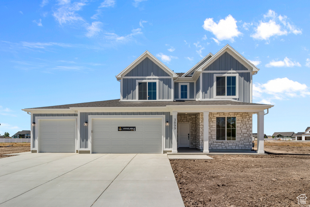 View of front facade featuring board and batten siding, concrete driveway, covered porch, an attached garage, and stone siding