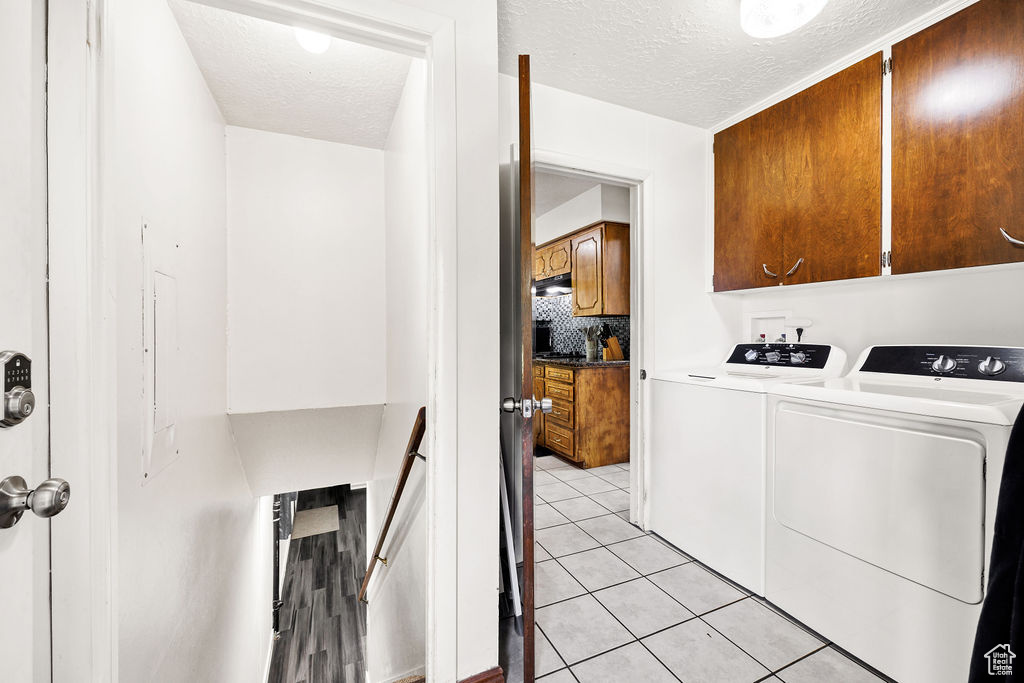 Washroom featuring cabinet space, independent washer and dryer, a textured ceiling, and light tile patterned floors