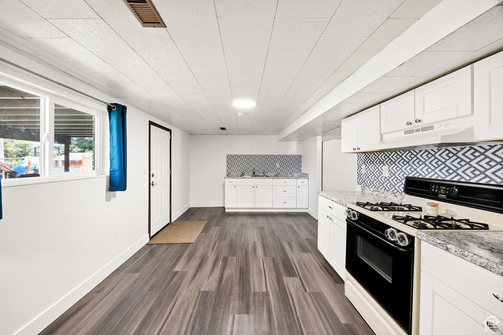 Kitchen featuring range with gas cooktop, under cabinet range hood, dark wood-style flooring, white cabinets, and backsplash