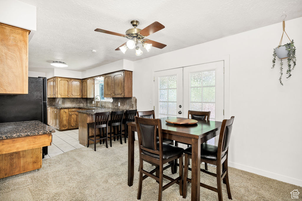 Dining space with ceiling fan, light carpet, french doors, a textured ceiling, and light tile patterned floors