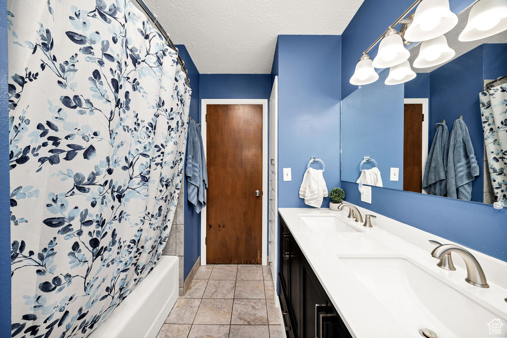 Bathroom with double vanity, shower / bath combo, and a textured ceiling