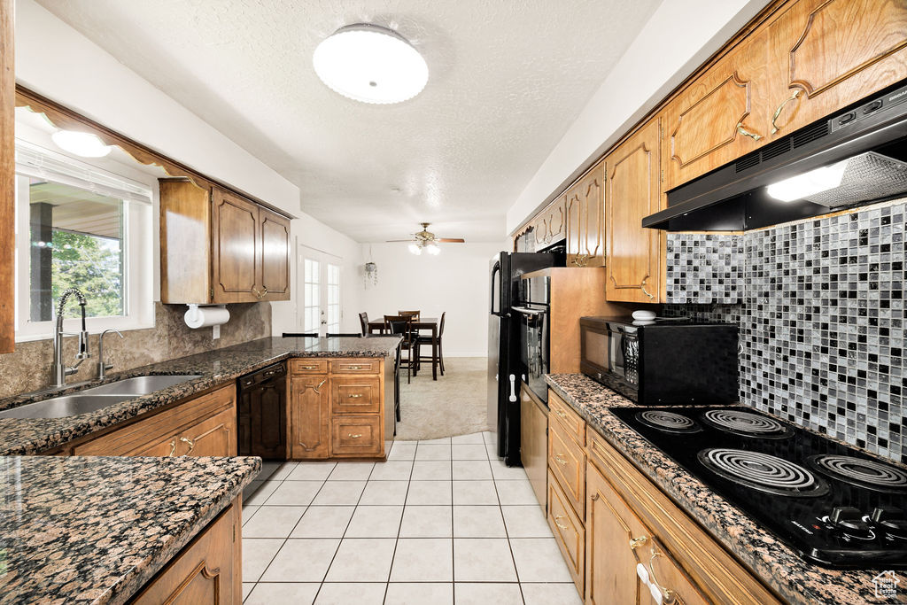 Kitchen featuring exhaust hood, black appliances, light tile patterned floors, tasteful backsplash, and a textured ceiling
