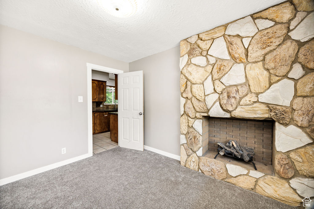 Unfurnished living room with carpet floors, a textured ceiling, and a stone fireplace