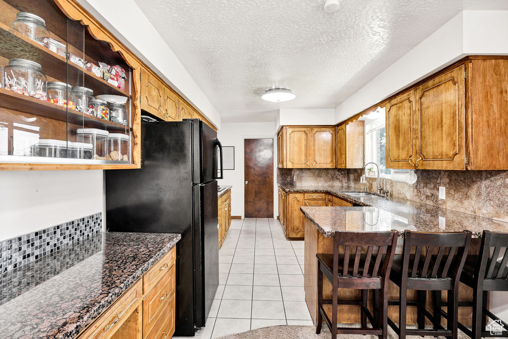 Kitchen featuring freestanding refrigerator, tasteful backsplash, a peninsula, dark stone countertops, and brown cabinetry