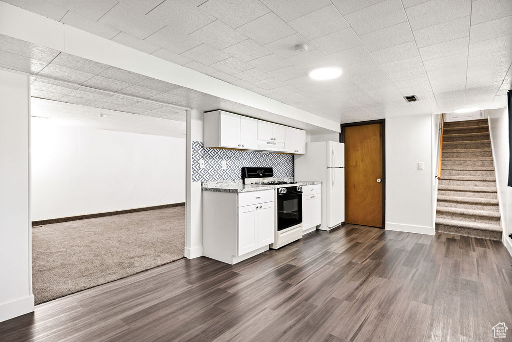 Kitchen with white appliances, white cabinetry, dark wood-style floors, and light stone counters