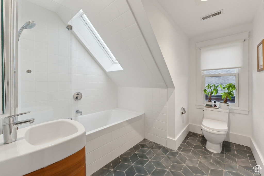 Bathroom featuring a skylight, tile patterned flooring, vaulted ceiling, tiled shower / bath, and vanity