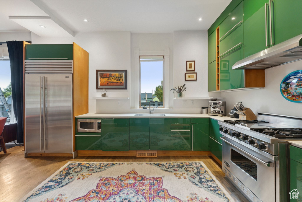 Kitchen with built in appliances, green cabinetry, light wood-type flooring, extractor fan, and light countertops