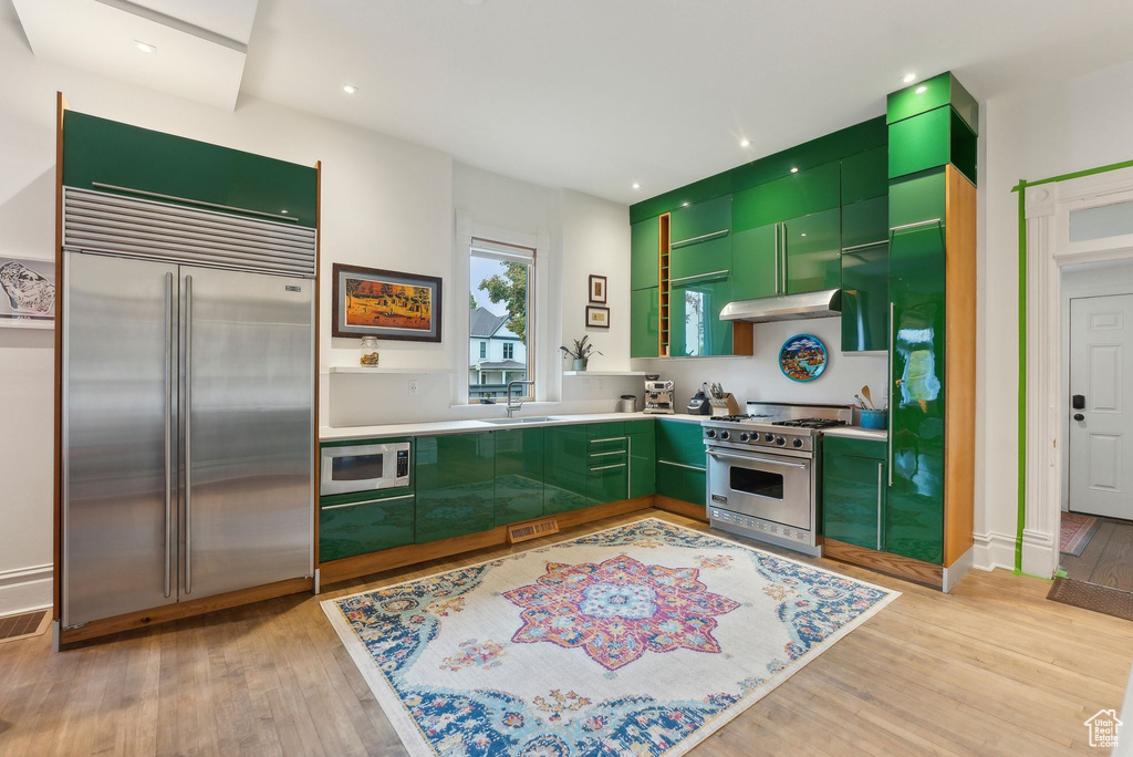 Kitchen with built in appliances, green cabinetry, light wood-style flooring, under cabinet range hood, and light countertops