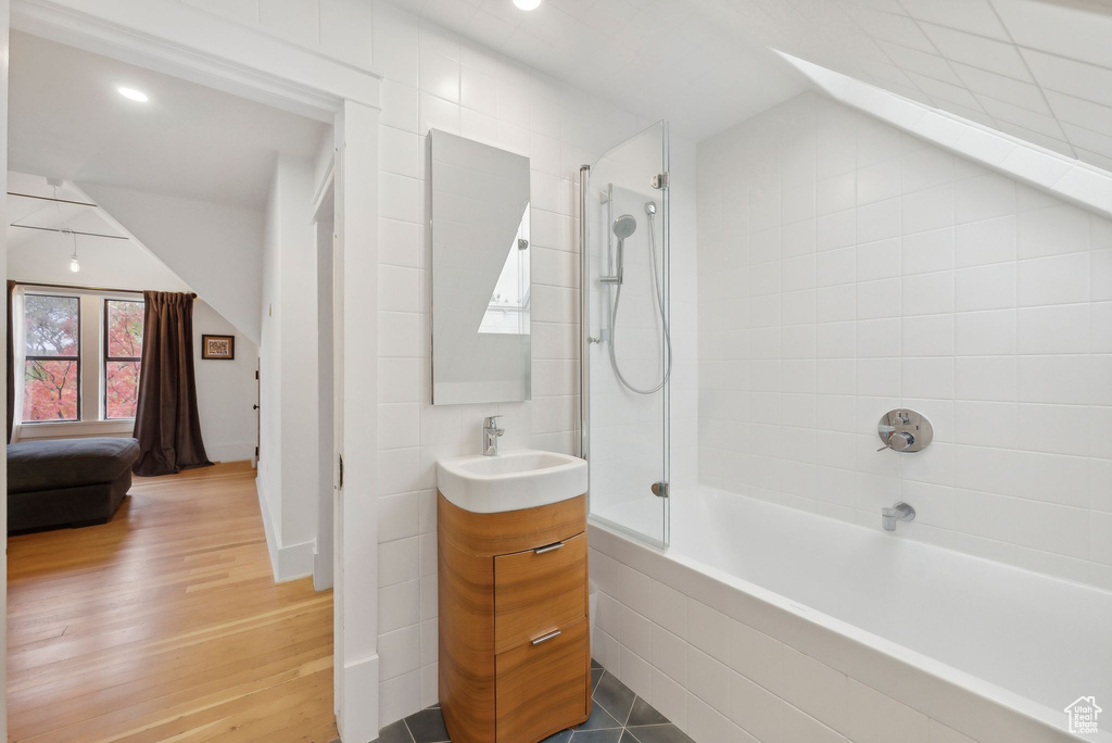Bathroom featuring vanity, shower / bath combination, wood finished floors, and lofted ceiling