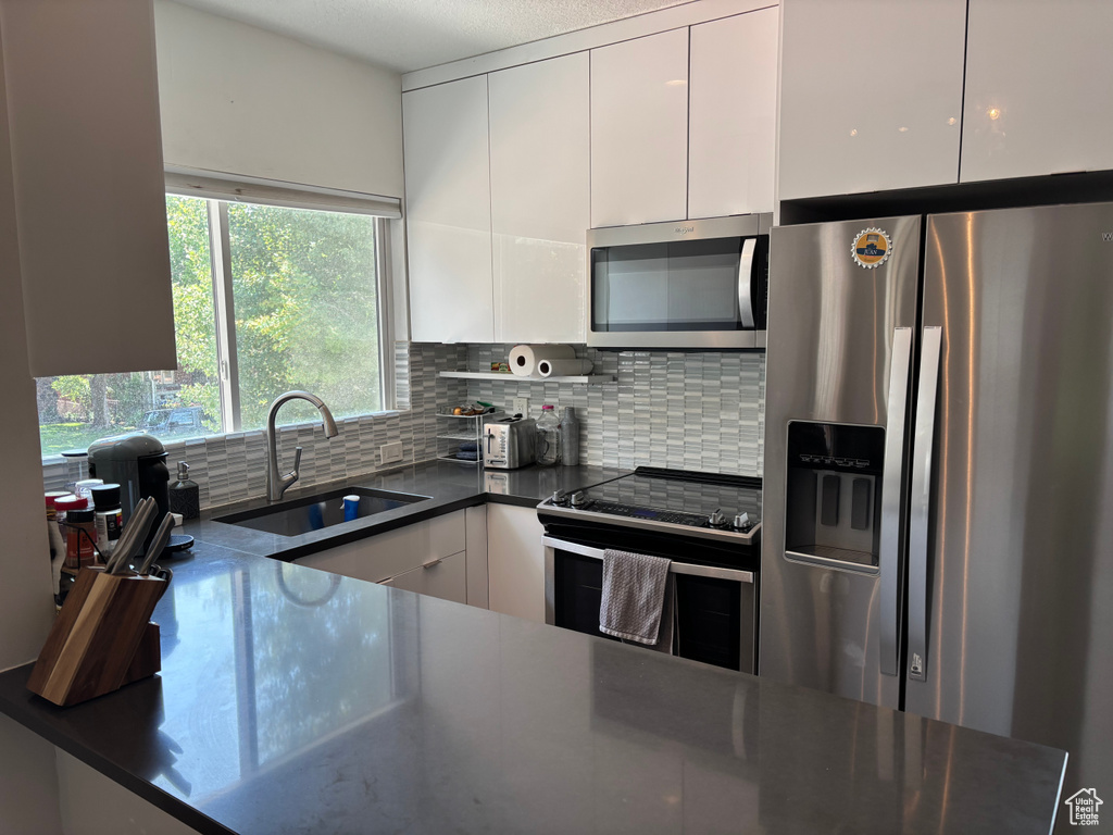 Kitchen featuring stainless steel appliances, dark countertops, white cabinetry, and decorative backsplash