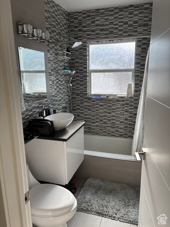 Bathroom with tile patterned flooring, tiled shower / bath combo, vanity, and tile walls