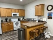 Kitchen with white appliances, brown cabinetry, and a breakfast bar