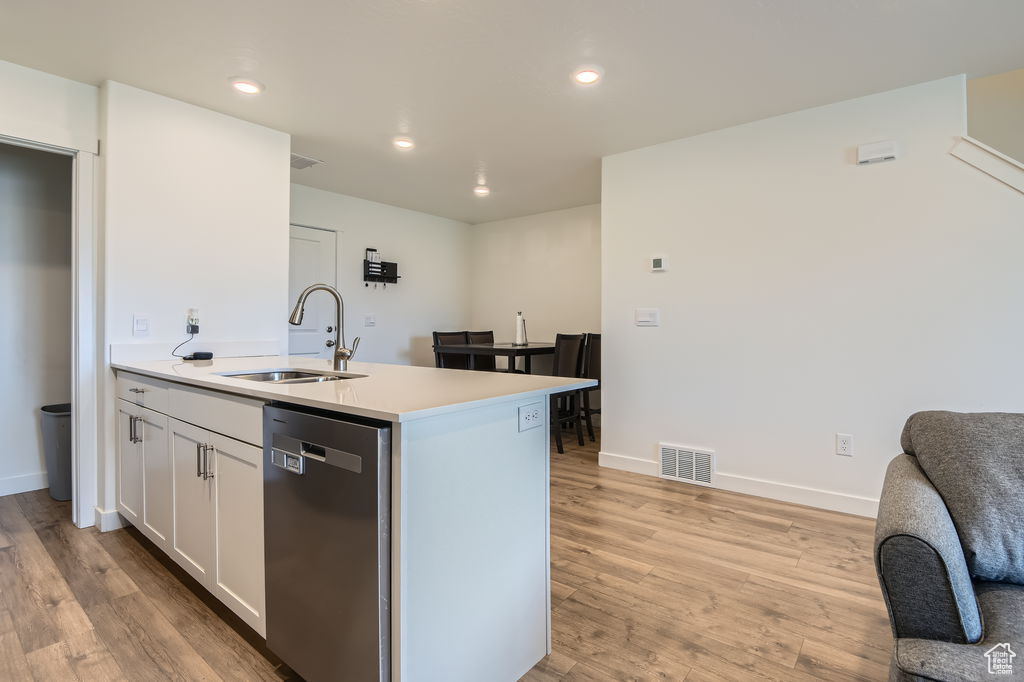 Kitchen featuring stainless steel dishwasher, light wood finished floors, light countertops, recessed lighting, and white cabinets