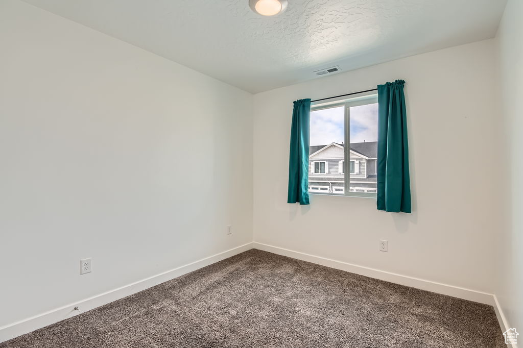 Empty room featuring dark colored carpet and a textured ceiling
