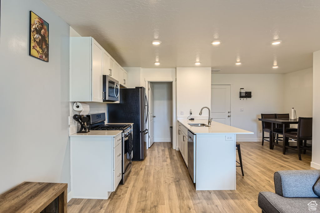 Kitchen featuring stainless steel appliances, a breakfast bar, light countertops, light wood-style flooring, and recessed lighting