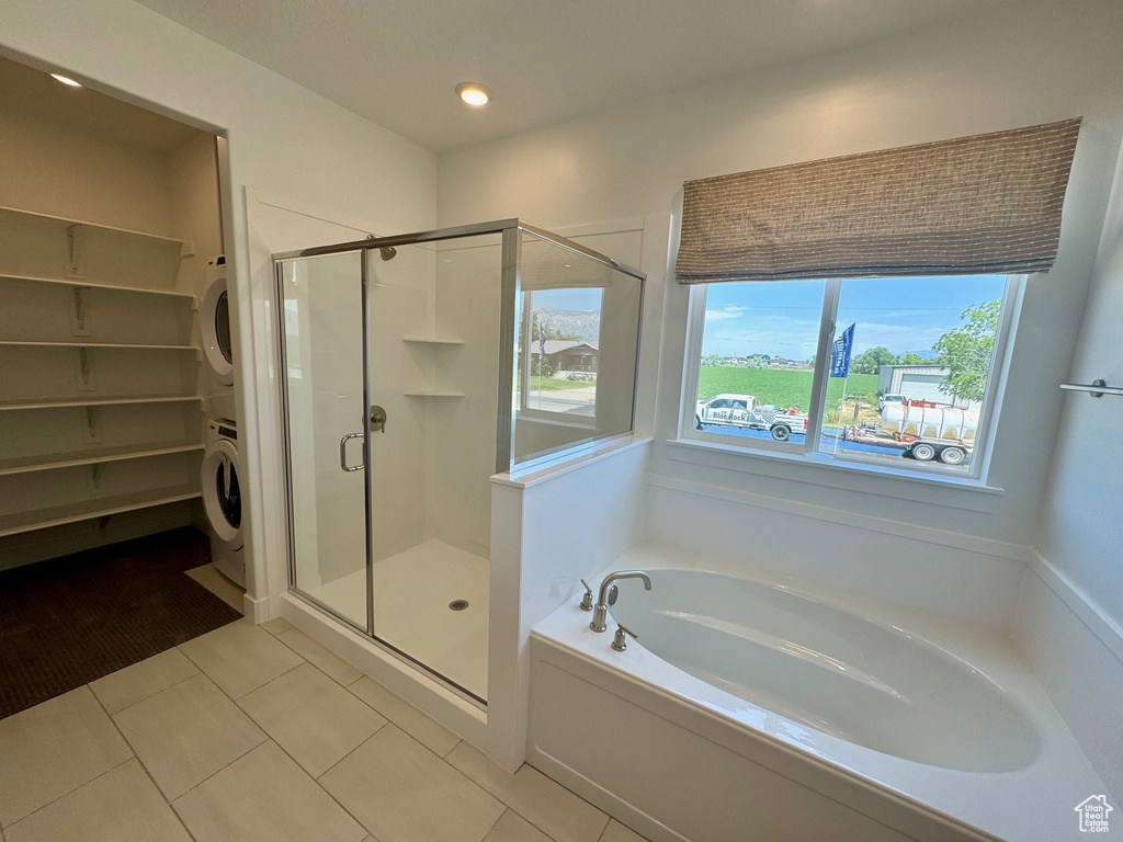 Full bath with stacked washer and clothes dryer, a garden tub, a stall shower, tile patterned floors, and a spacious closet