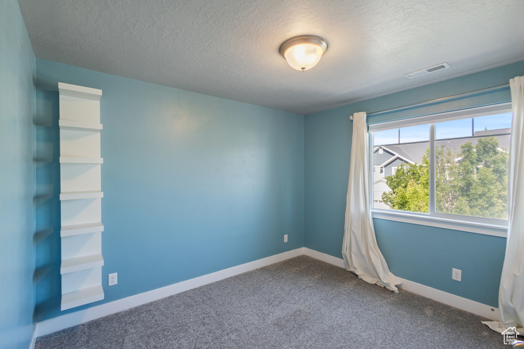 Spare room featuring a textured ceiling and dark carpet