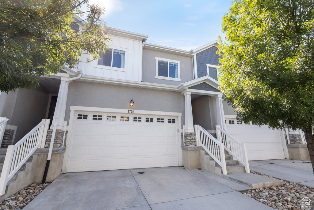 View of front of property featuring an attached garage, stone siding, driveway, and stucco siding