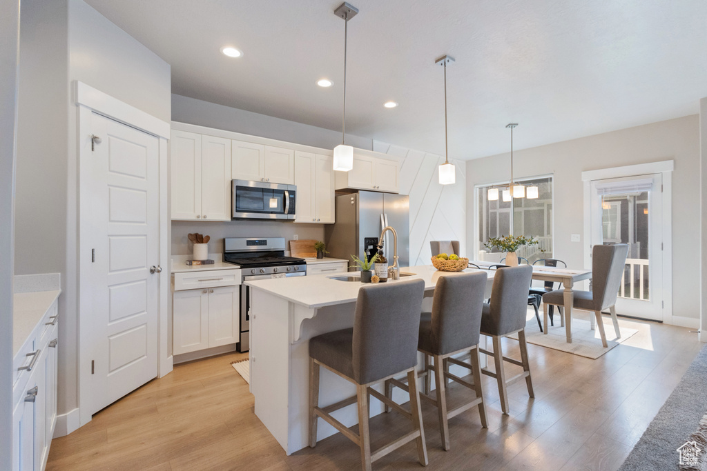 Kitchen featuring appliances with stainless steel finishes, light wood-style flooring, a center island with sink, a breakfast bar, and recessed lighting