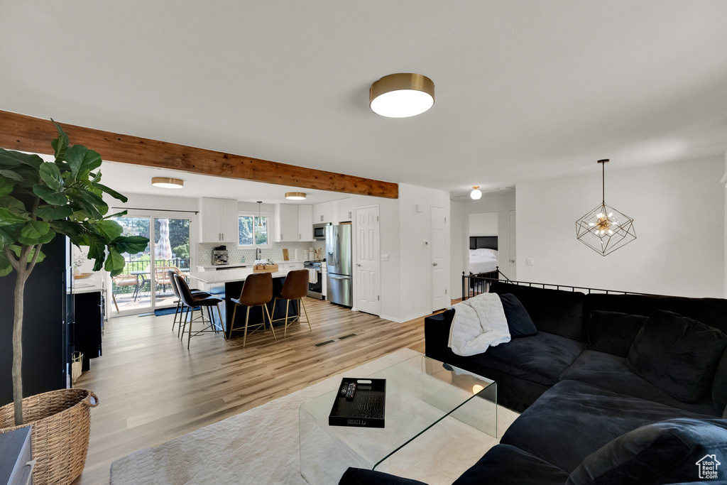 Living area with light wood-style floors, beam ceiling, and a chandelier