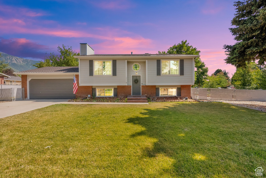 Split foyer home featuring driveway, a chimney, brick siding, and a garage