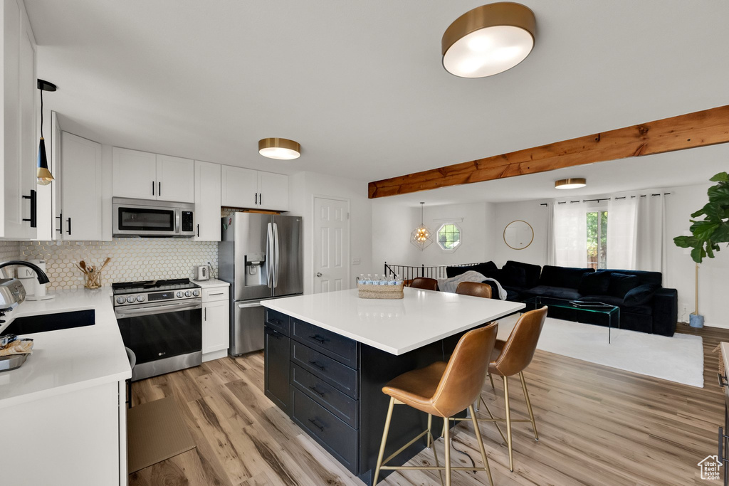 Kitchen featuring stainless steel appliances, a kitchen breakfast bar, light wood finished floors, light countertops, and white cabinets