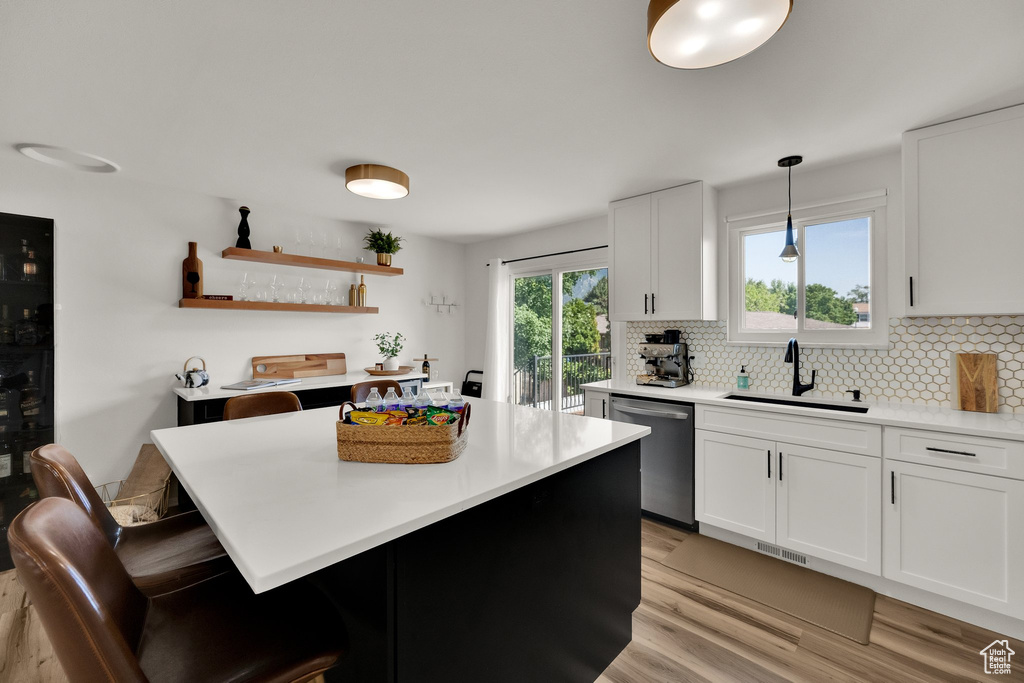 Kitchen with dishwasher, light wood-style flooring, backsplash, light countertops, and a kitchen bar